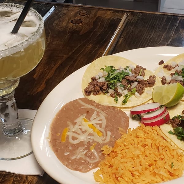 Mexican plate with beef tacos, refried beans, rice, salsa, radishes, and lime beside a salted margarita.